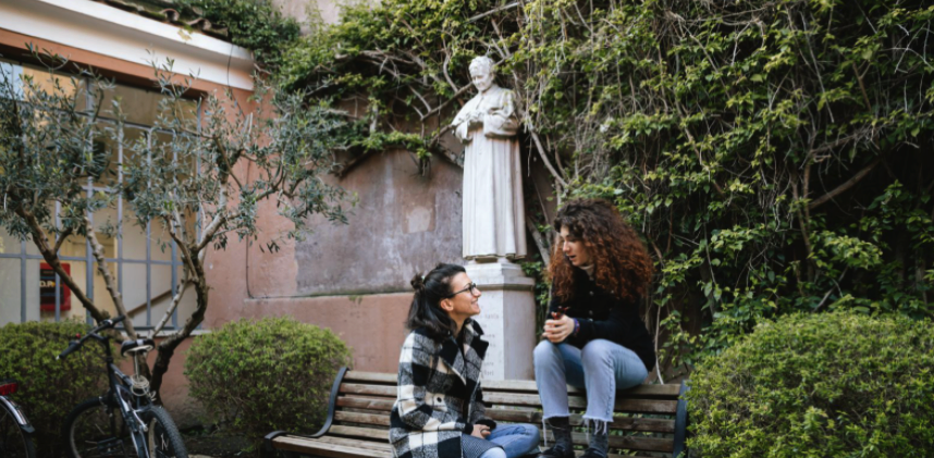 Two girls sit on a bench in front of a statue